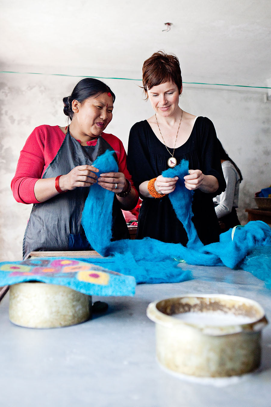 Jennifer Pulling and a woman smile while inspecting blue dyed felt