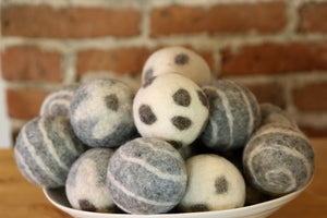 Various dryer balls with different colours and patterns stacked in a  large bowl on a counter